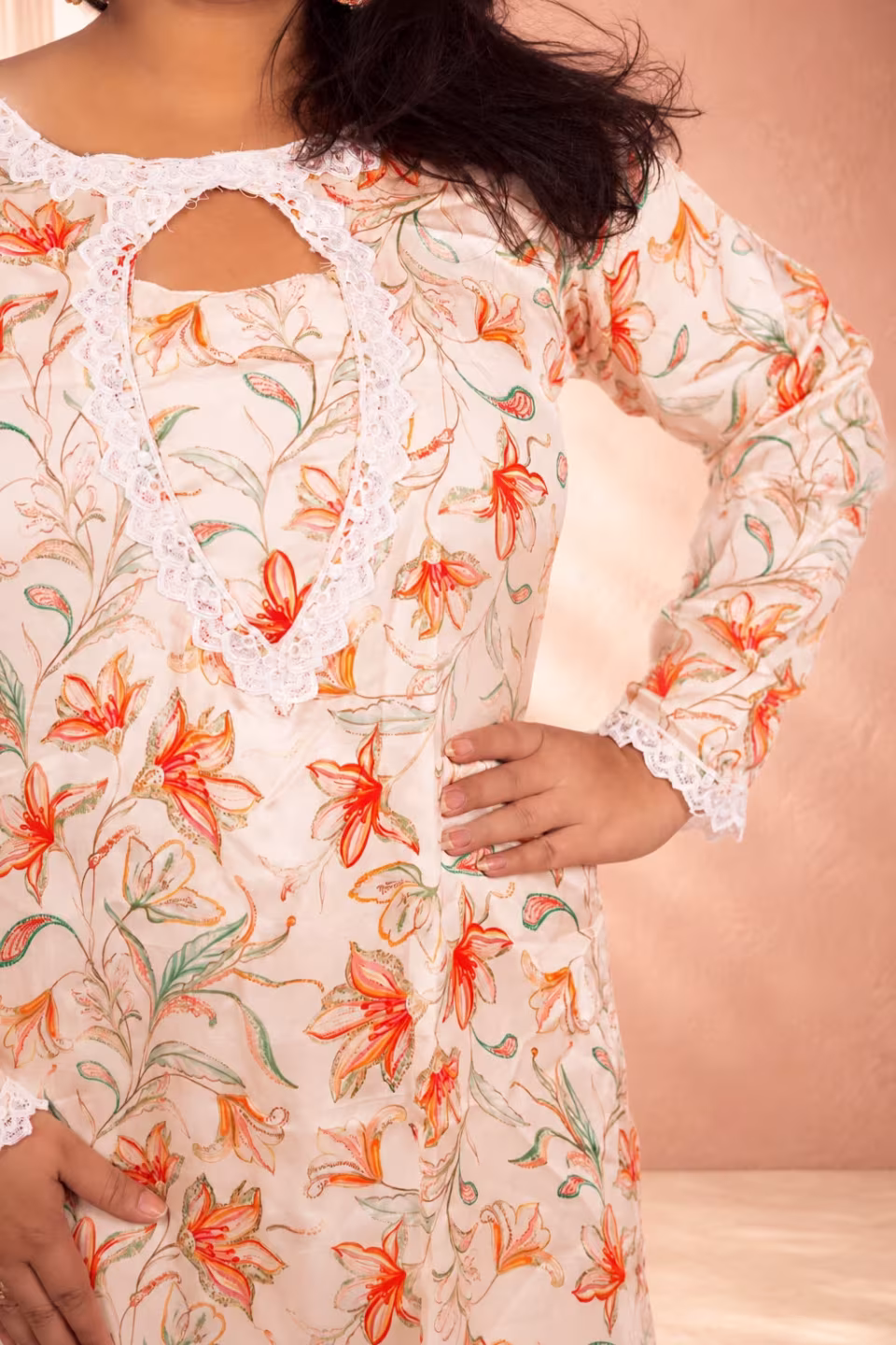 Close-up of the intricate peach and orange floral print and delicate white lace detailing on the sleeve of a cream floral silk kurti.