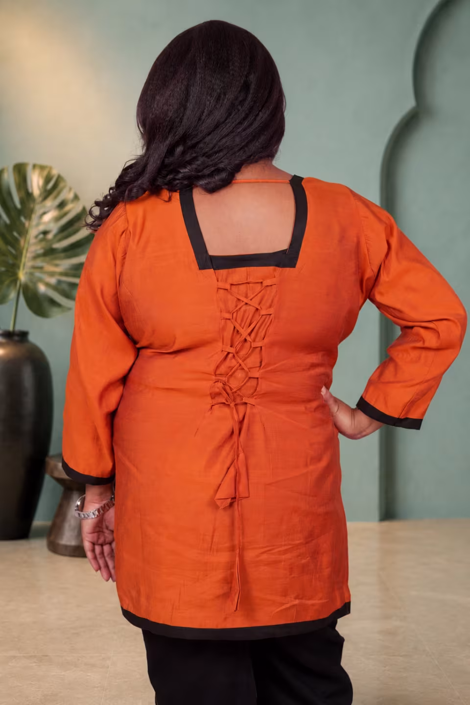 Back view of an orange kurti showcasing a deep square neckline with black borders and a criss-cross tie-up detail.