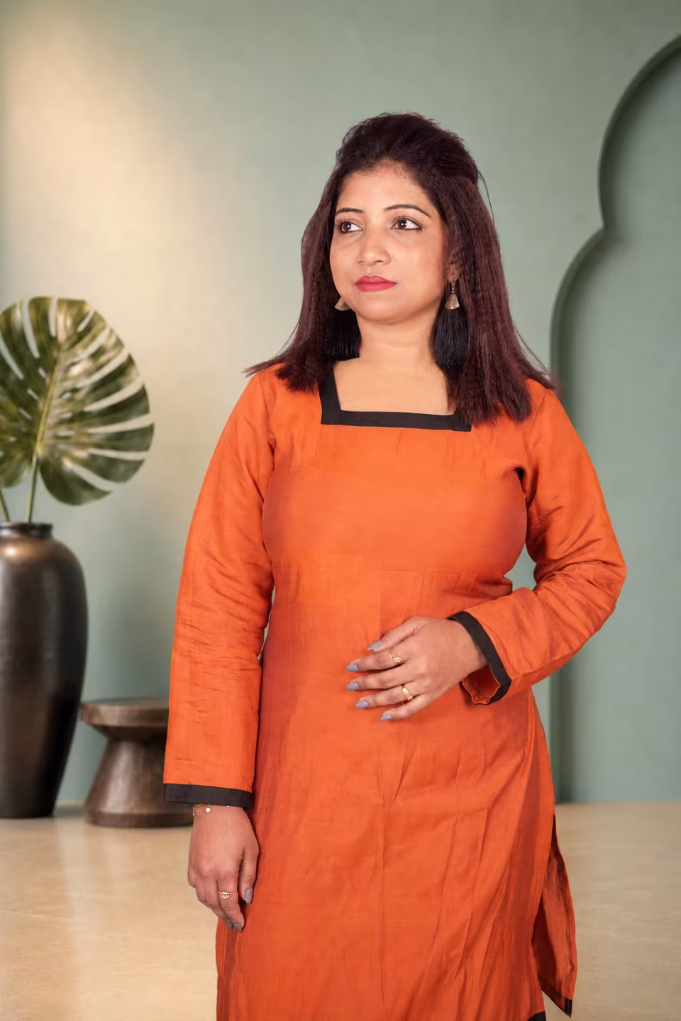 Woman modeling a vibrant orange square neck kurti with black contrast borders looking off-camera.