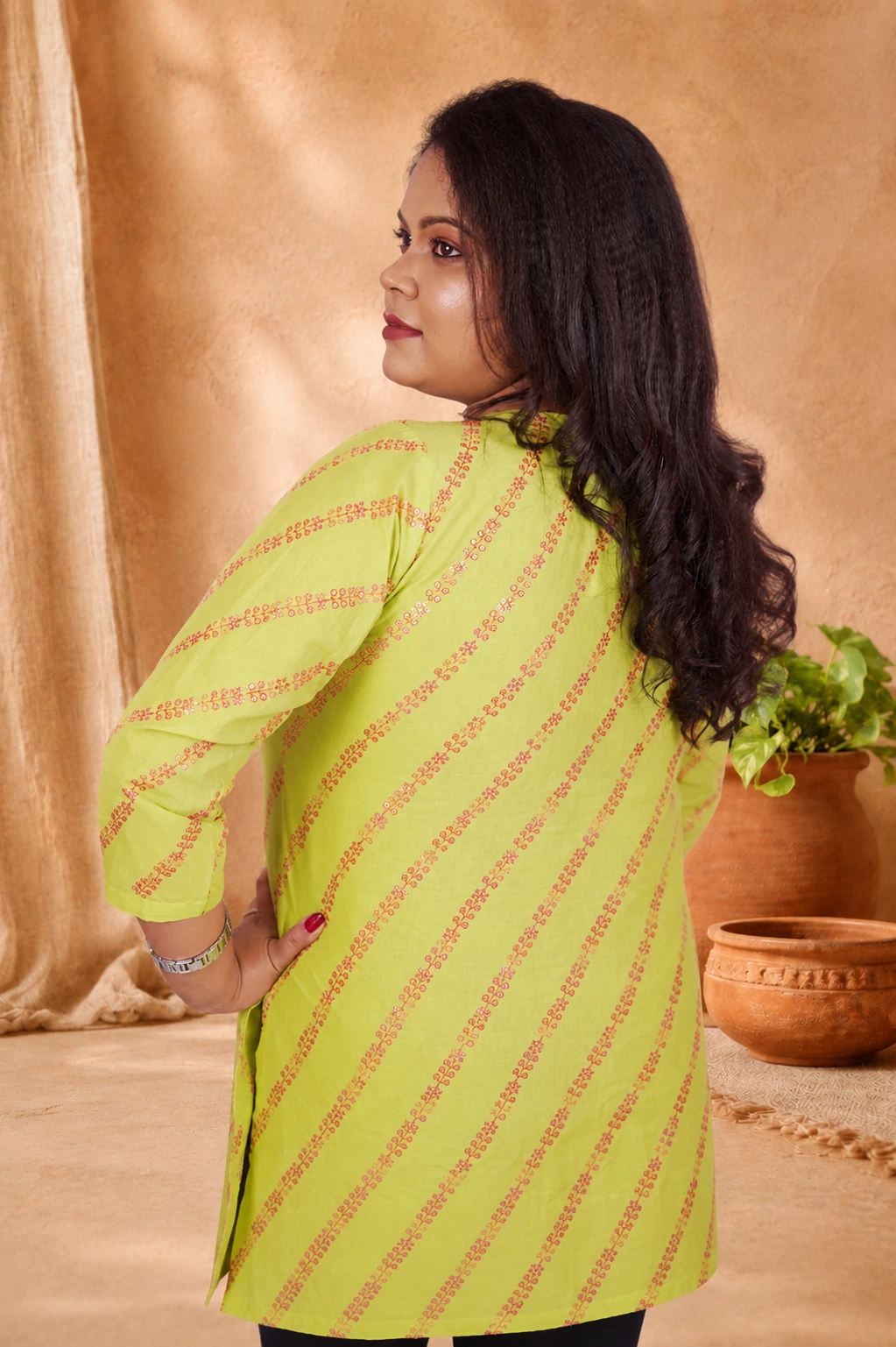 Angled back view of lime green cotton kurti with sequin stripe print and black pants